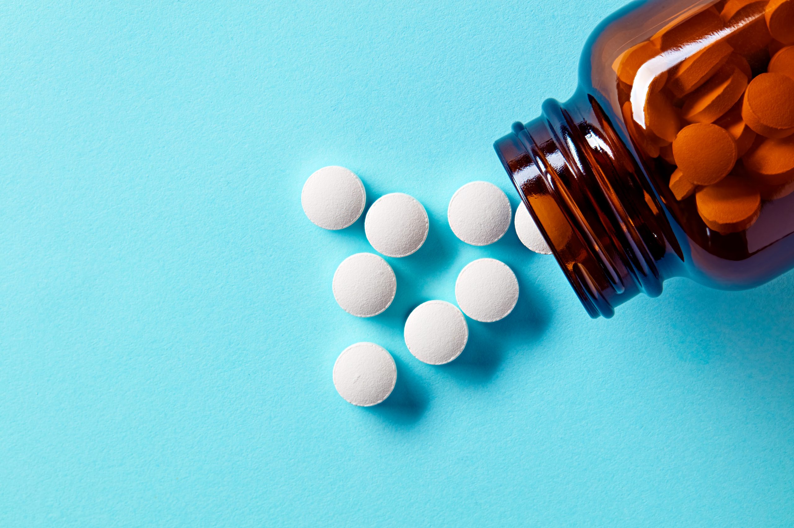 Bottle of pills spilling across bright blue surface.