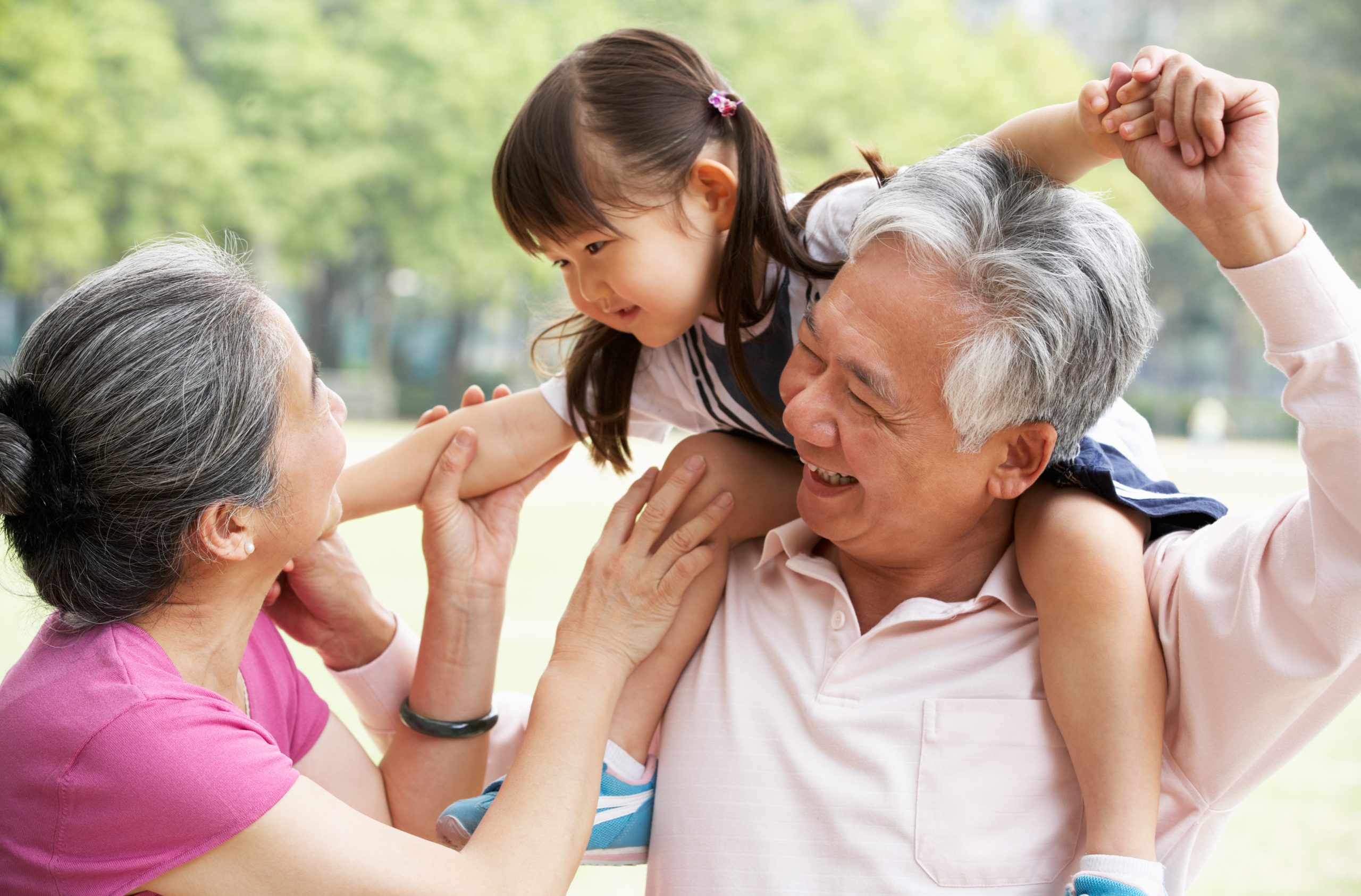 Grandparents play with their granddaugther outdoors.