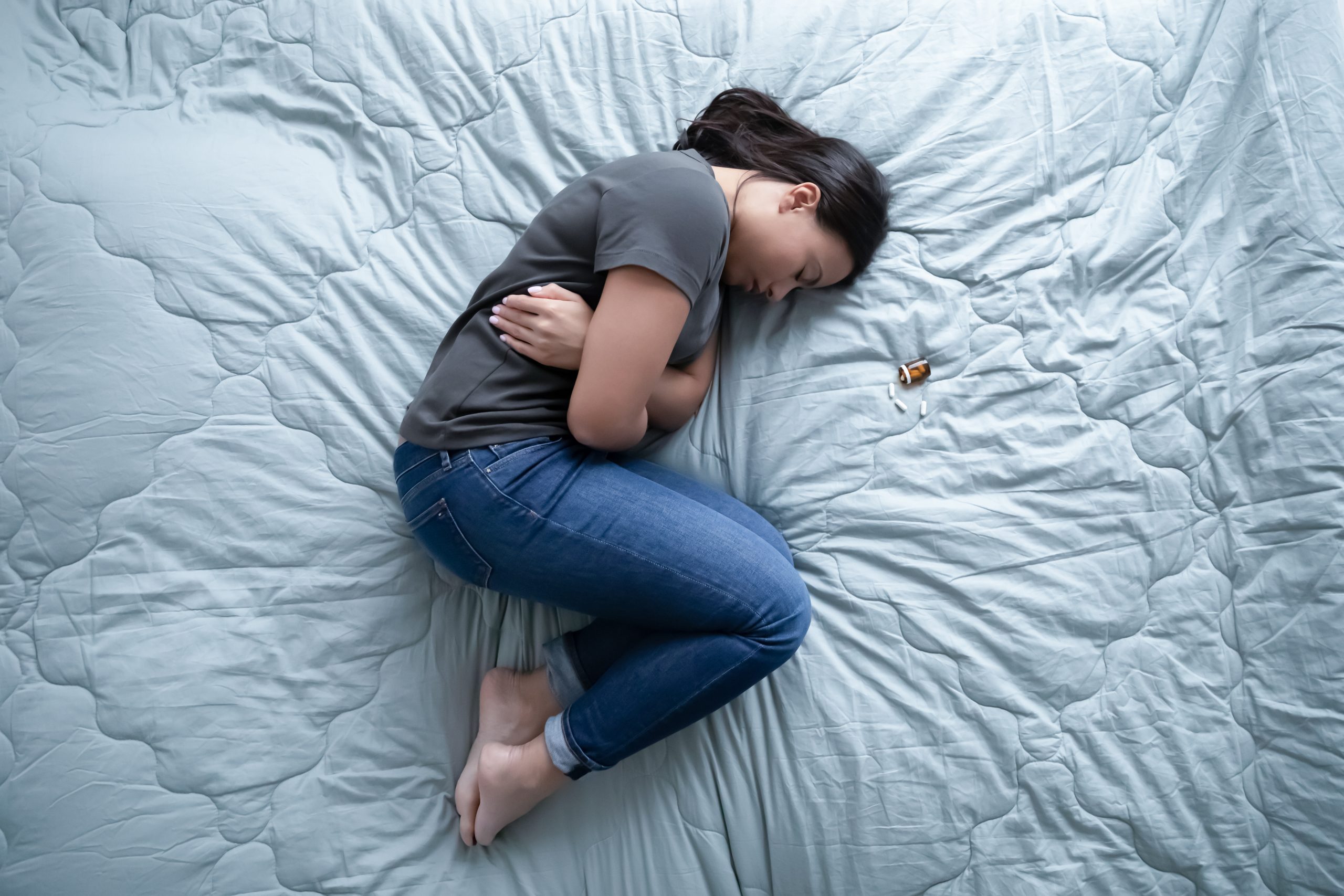 Teenager curled up on bed next to pill bottle